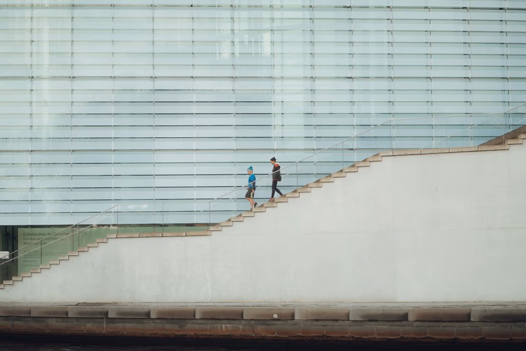 Two people ascending a modern staircase against a glass facade in Berlin, Germany.