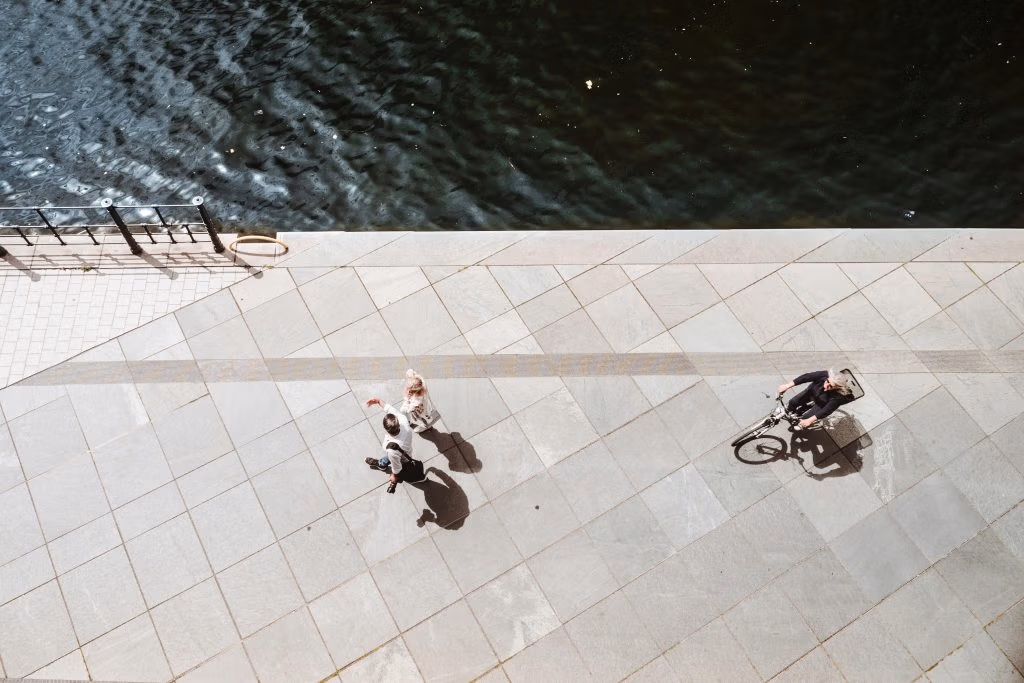 Overhead shot of a cyclist and pedestrians alongside a river in Berlin, showcasing daily life.